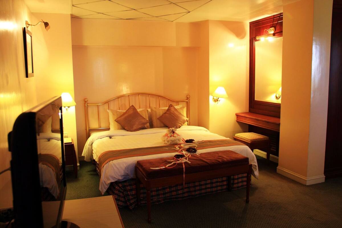 A hotel room with a bed, bedside lamps, a mirror, a bench, and a dresser.
