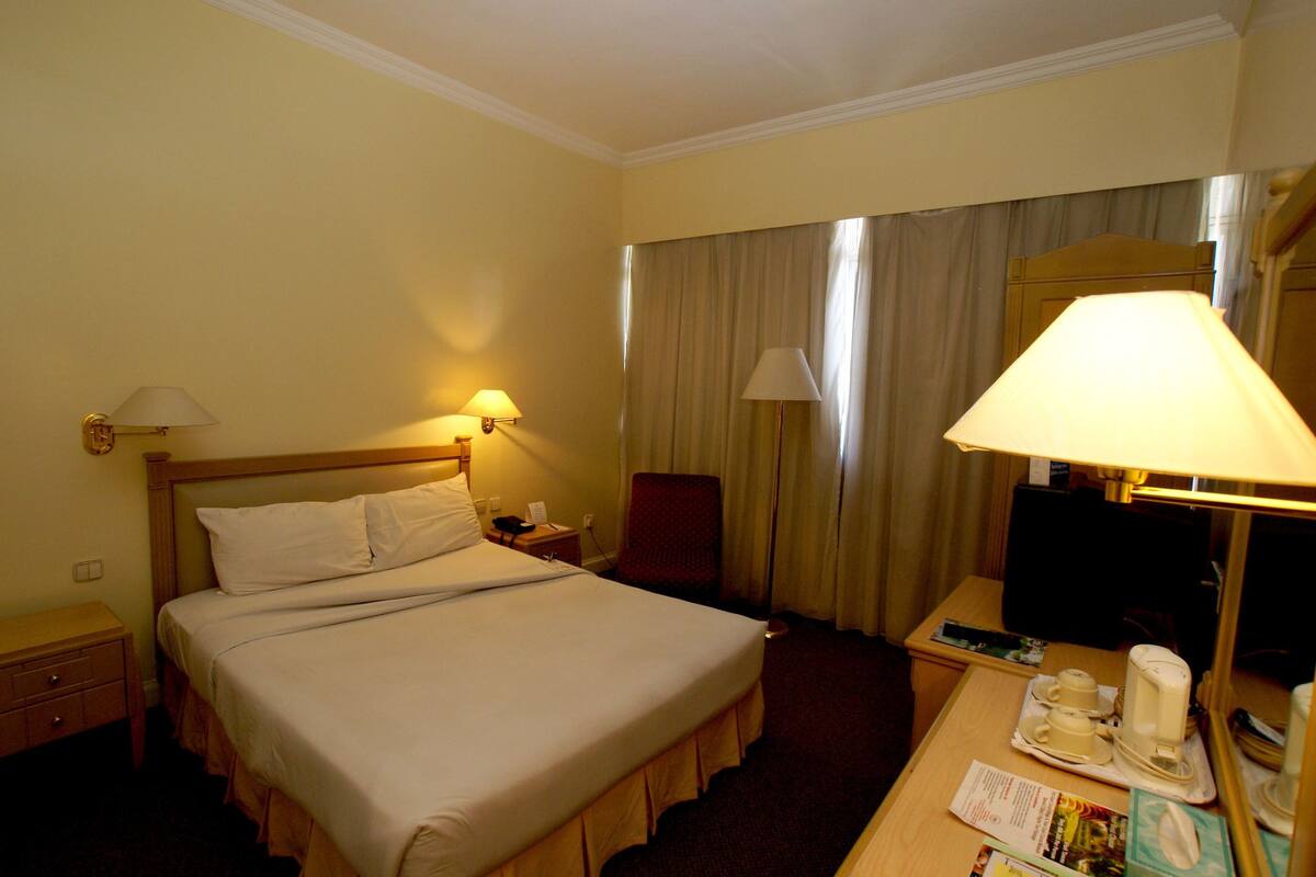 A hotel room with a large bed, two bedside lamps, a desk with a telephone, a chair, and a television.