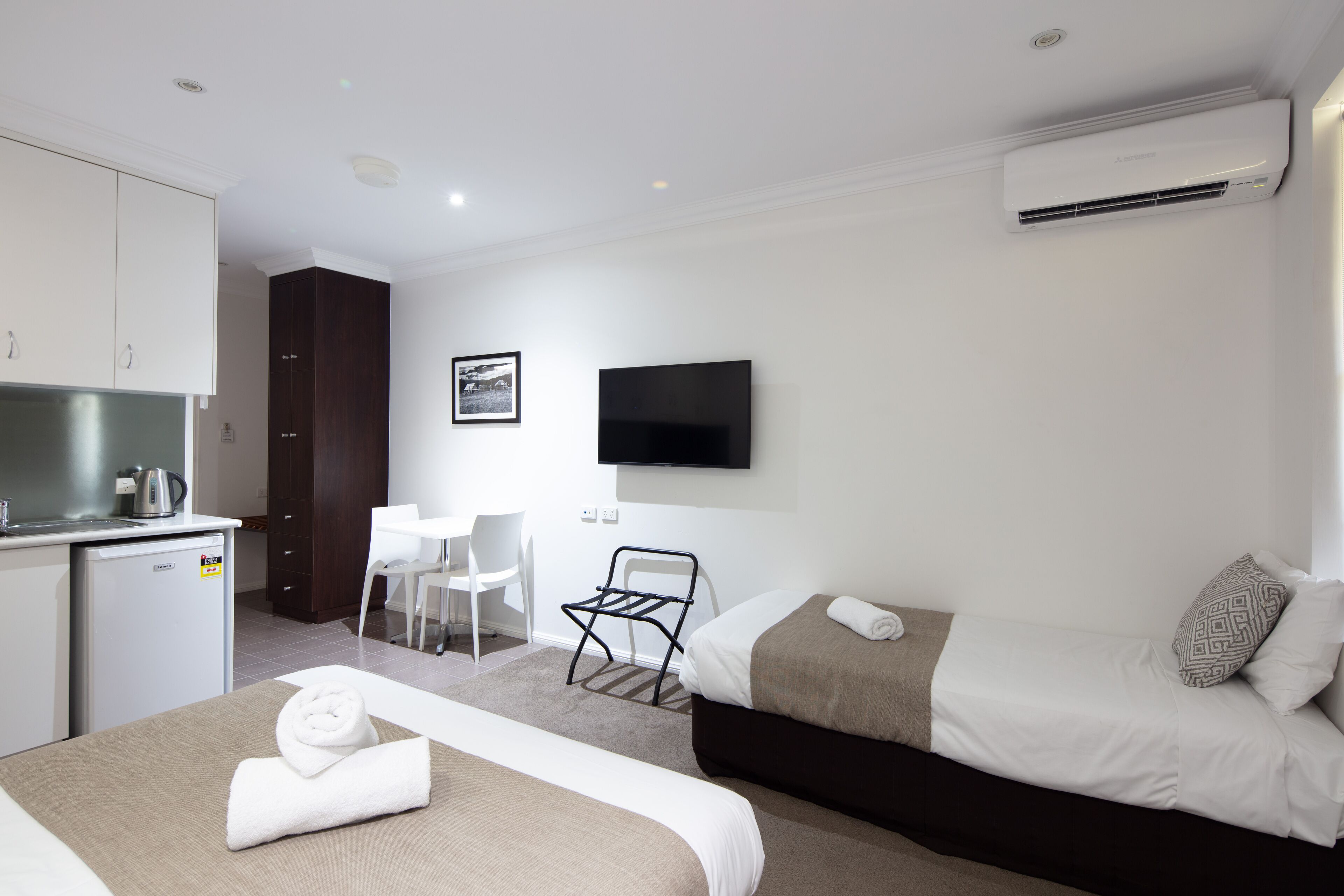 Una camera d'albergo con un letto, una scrivania, una sedia, un angolo cottura e una TV a muro.