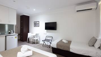 Una camera d'albergo con un letto, una scrivania, una sedia, un angolo cottura e una TV a muro.