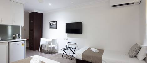 Habitación de hotel con cama, escritorio, silla, kitchenette pequeño y televisor montado en la pared.