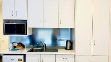 A compact kitchen with white cabinets, a microwave, a sink, and a small refrigerator.