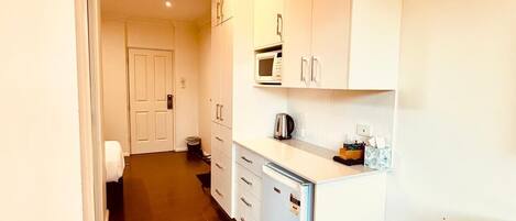 Cocina compacta con armarios blancos, un microondas y un refrigerador pequeño.