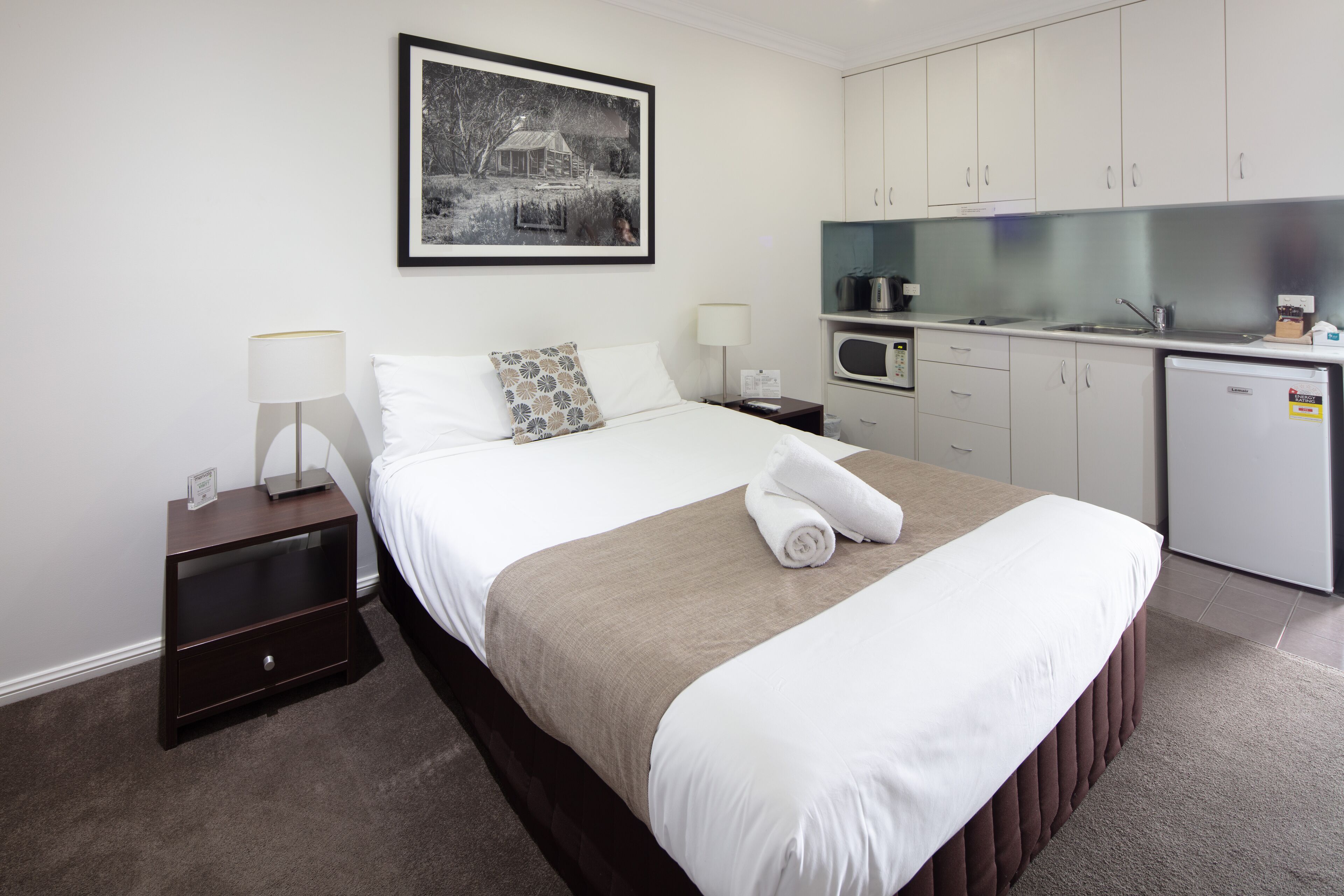 Una habitación de hotel con una cama, una mesita de noche, un escritorio, un microondas y un refrigerador.