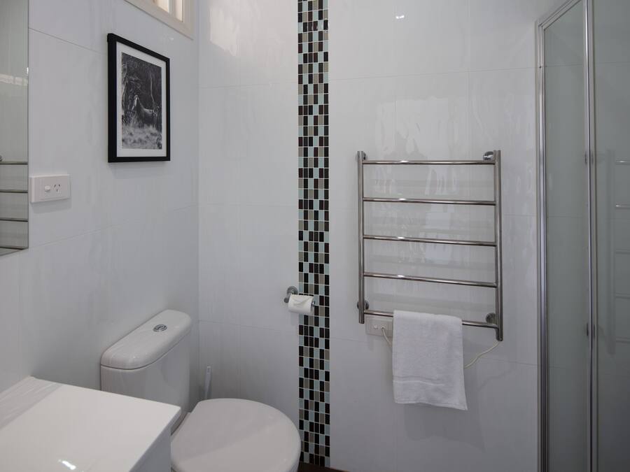 Un baño moderno con inodoro, lavamanos, cabina de ducha de vidrio y toallero.