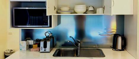 Una kitchenette compacta con microondas, lavabo y alacenas.