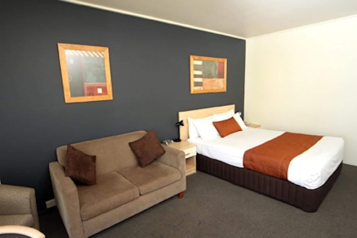 A hotel room with a bed, a sofa, and two framed pictures on the wall.