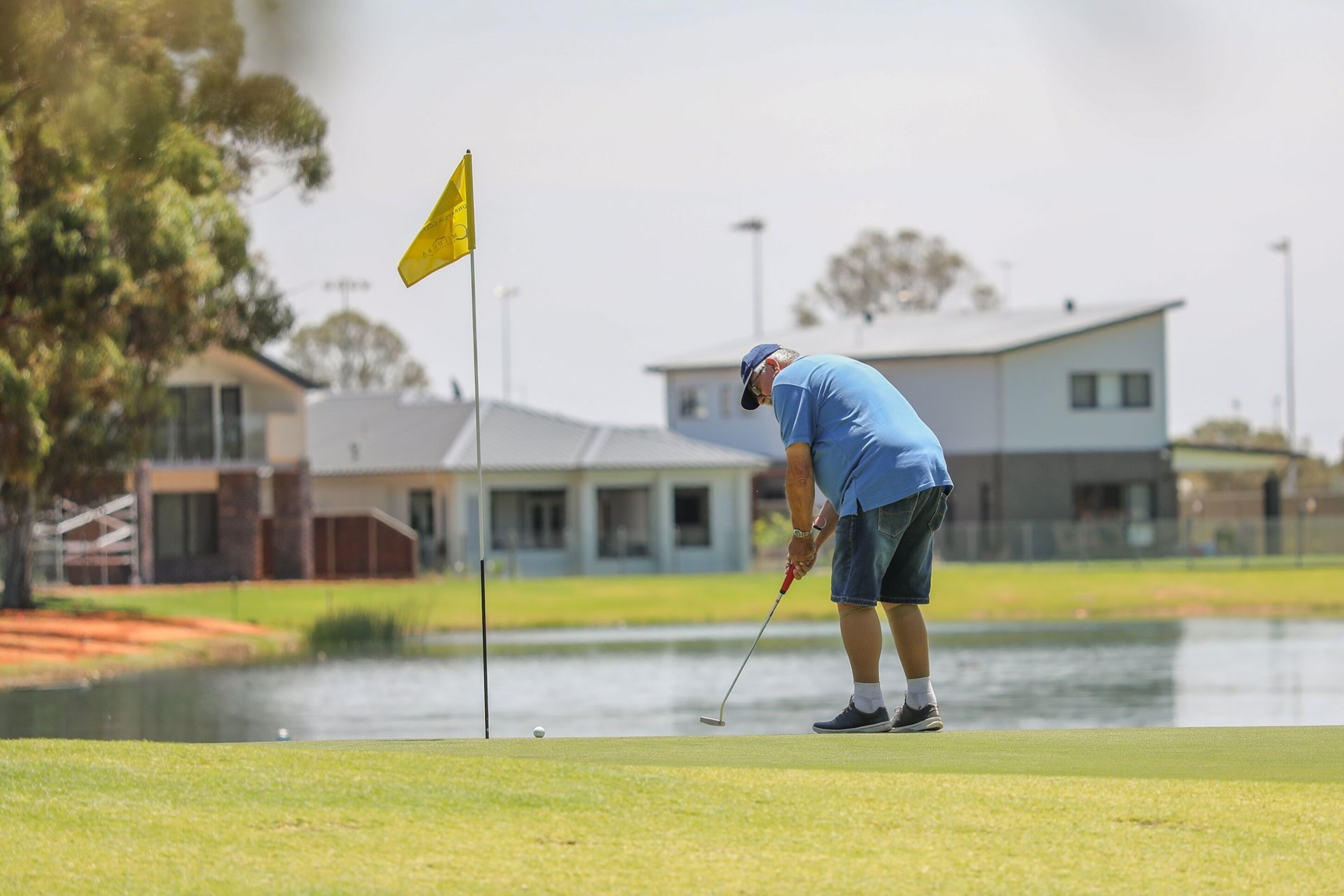 A person on a golf course near a body of water, with a building in the background.