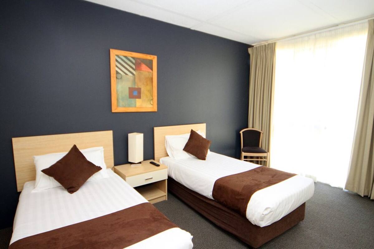 A hotel room with two beds, a nightstand, a chair, and a painting on the wall.
