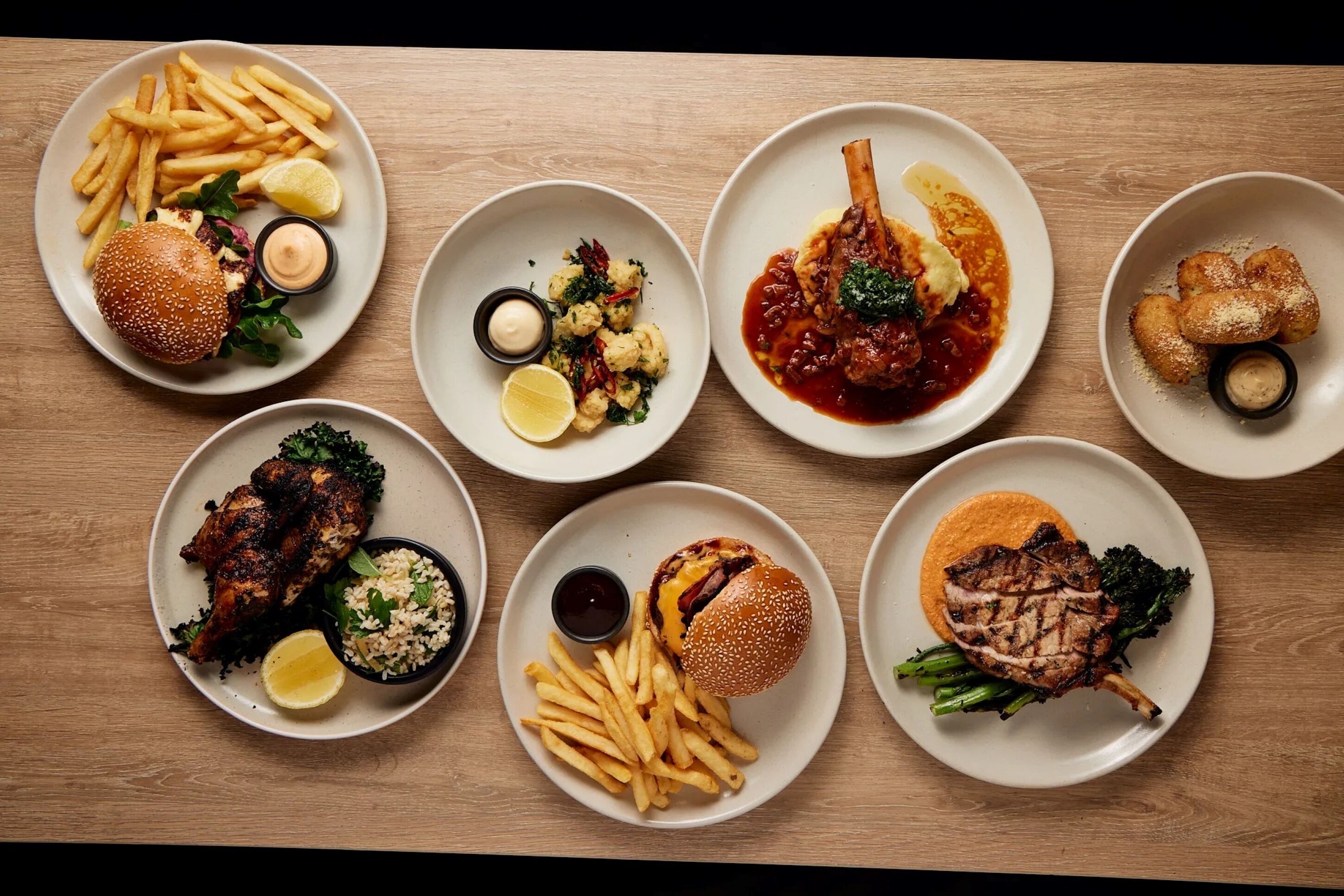 Variedad de platos con hamburguesas, papas fritas y otros alimentos, colocados sobre una mesa de madera.