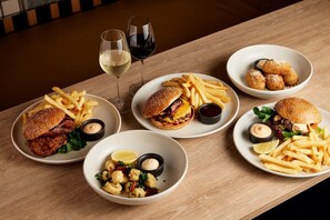 Ett bord fyllt med olika rätter, inklusive hamburgare, pommes frites och skaldjur, och till det serveras glas med vin.