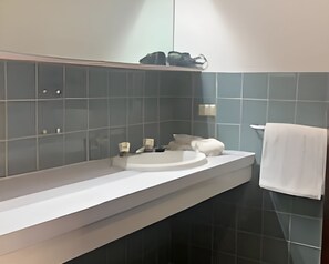 Ett modernt badrum med en vit bänkskiva, ett handfat och en spegel. Det står två flaskor på bänkskivan och en handduk hänger på väggen.