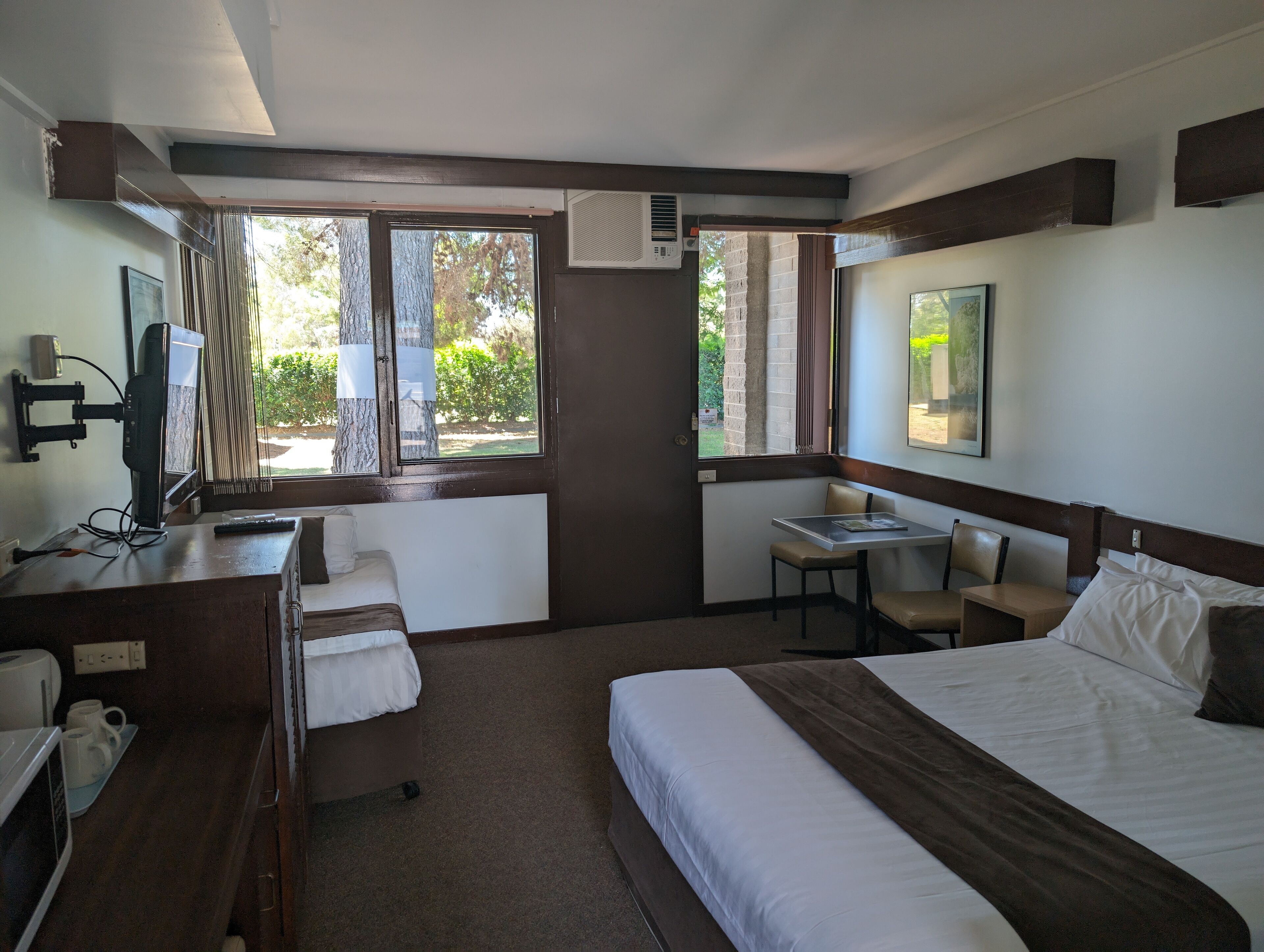 Hotelkamer met een bed, bureau met computer, stoel, klein tafeltje en raam met uitzicht op groen.