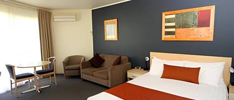 Habitación de hotel con cama, escritorio, silla, sofá y dos cuadros en la pared.