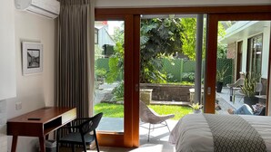 Ein Schlafzimmer mit Bett, Schreibtisch und Stuhl. Eine Glastür führt in einen Garten.