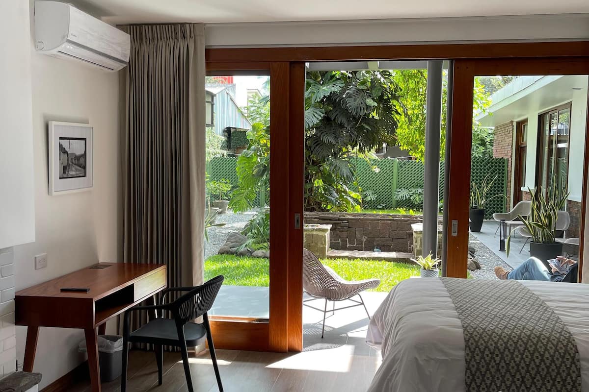 Ein Schlafzimmer mit Bett, Schreibtisch und Stuhl. Eine Glastür führt in einen Garten.