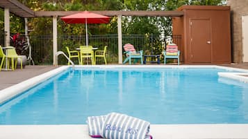 A swimming pool with a towel labeled "Bilexi, MS" on the edge, surrounded by colorful chairs and a red umbrella.