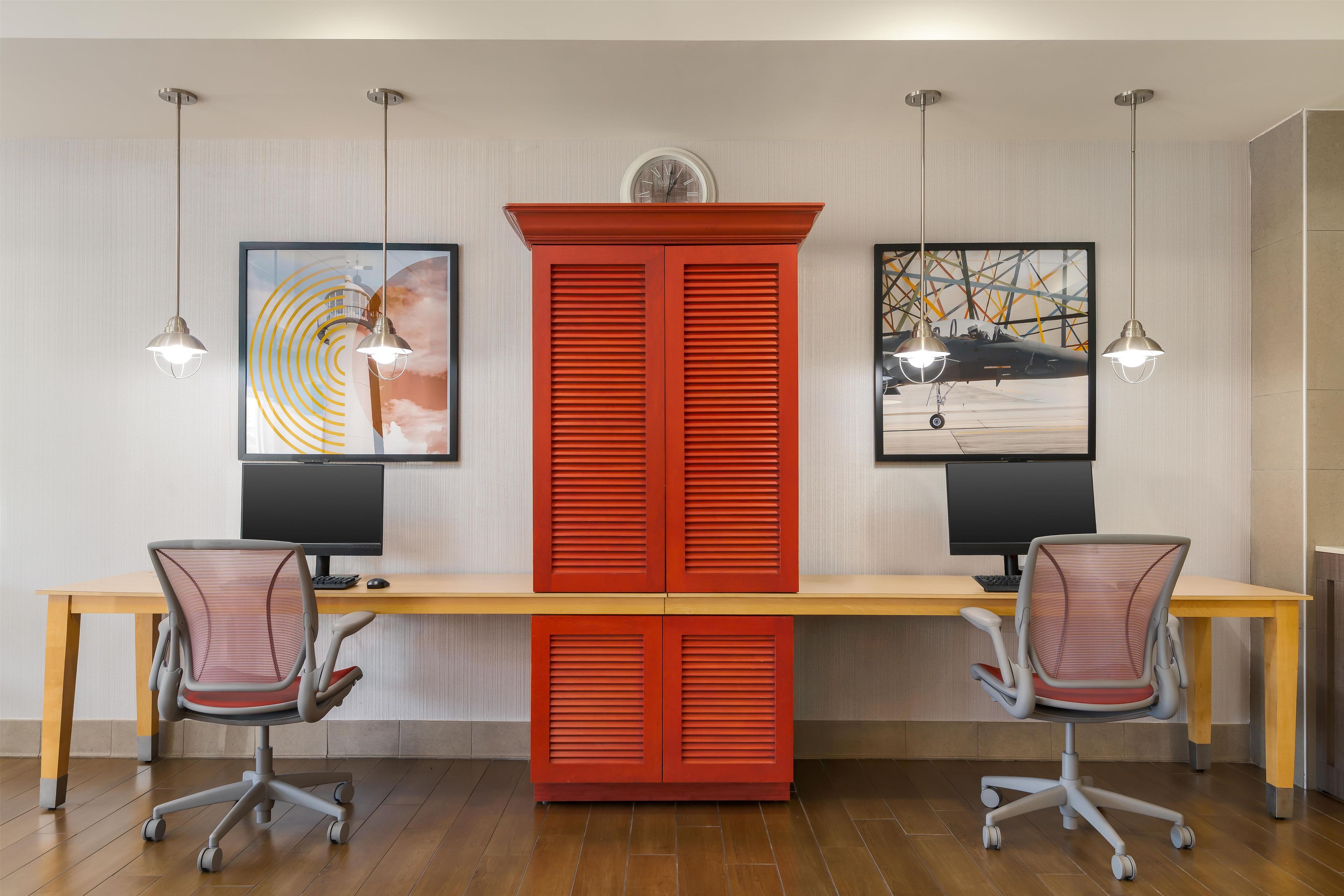 A modern office space with a long desk, two office chairs, and two pendant lights.