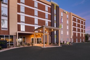 A modern hotel with a covered entrance, multiple floors, and an American flag. - Home2 Suites by Hilton Biloxi North/D'Iberville (D'Iberville)