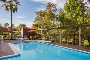 A pool area with a clear blue pool, surrounded by green chairs and tables, and a covered seating area with red umbrellas. - Home2 Suites by Hilton Biloxi North/D'Iberville (D'Iberville)