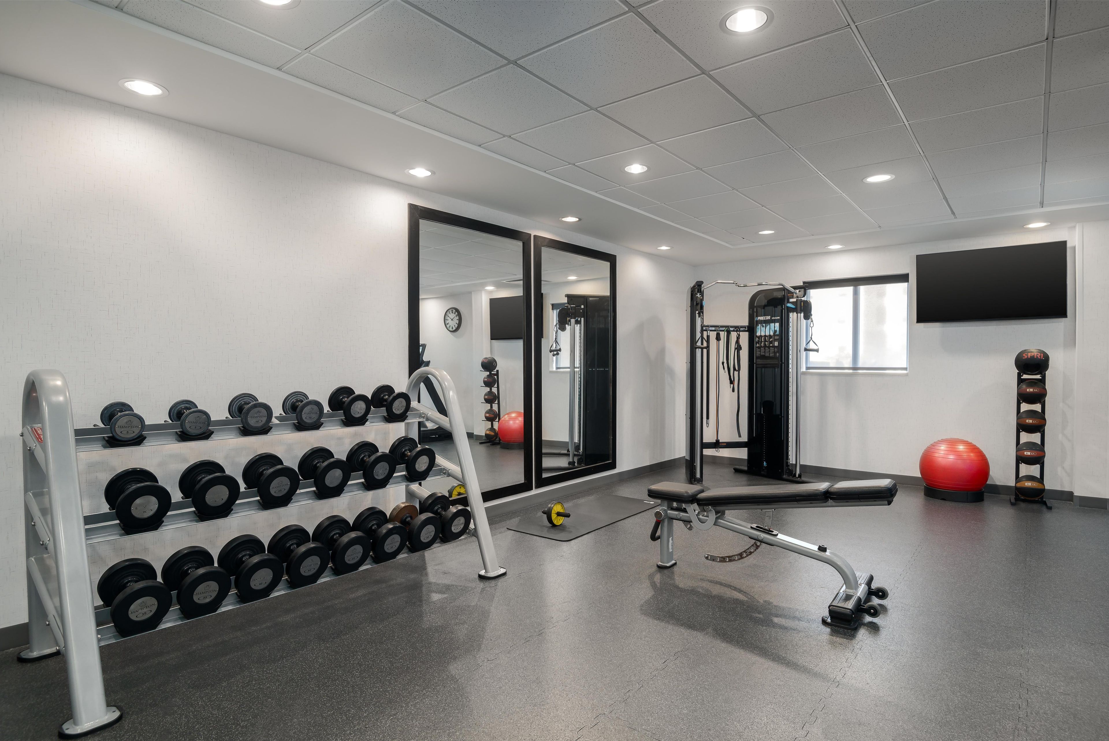 A gym with weightlifting equipment, a bench, and exercise balls.