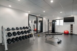 Un gimnasio con equipamiento de levantamiento de pesas, una banca y pelotas de ejercicio.
