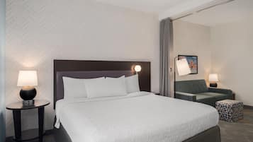 A hotel room with a large bed, two bedside tables with lamps, a sofa, and a patterned wall.