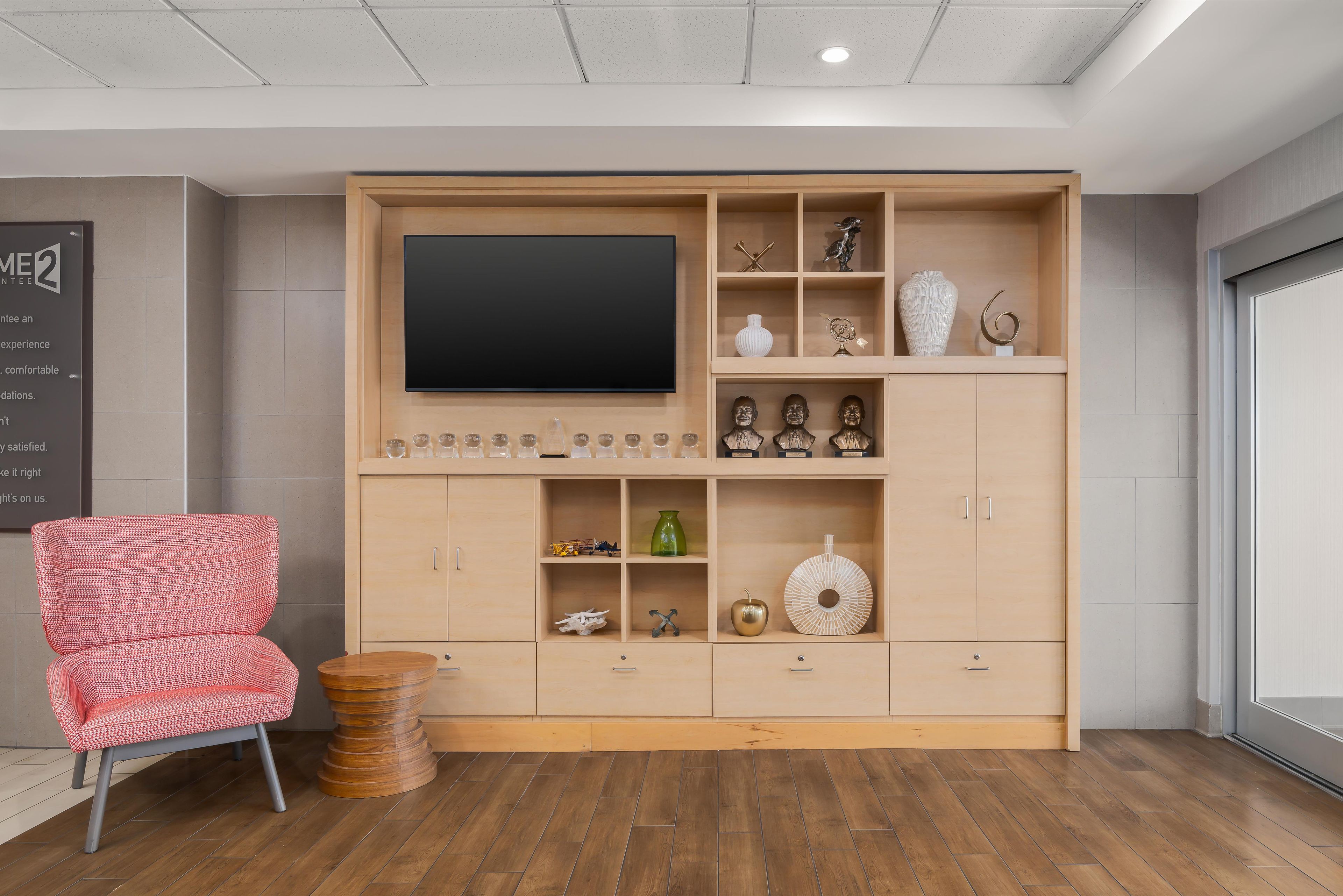 A modern living room with a large flat-screen TV, wooden shelving with decorative items, a red patterned chair, and a round wooden coffee table.