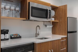 Una cocina moderna con microondas integrado, pileta de acero inoxidable y muebles de madera.