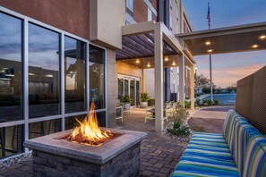 An outdoor seating area with a fire feature, a covered patio, and a view of the building's exterior. - Home2 Suites by Hilton Biloxi North/D'Iberville (D'Iberville)