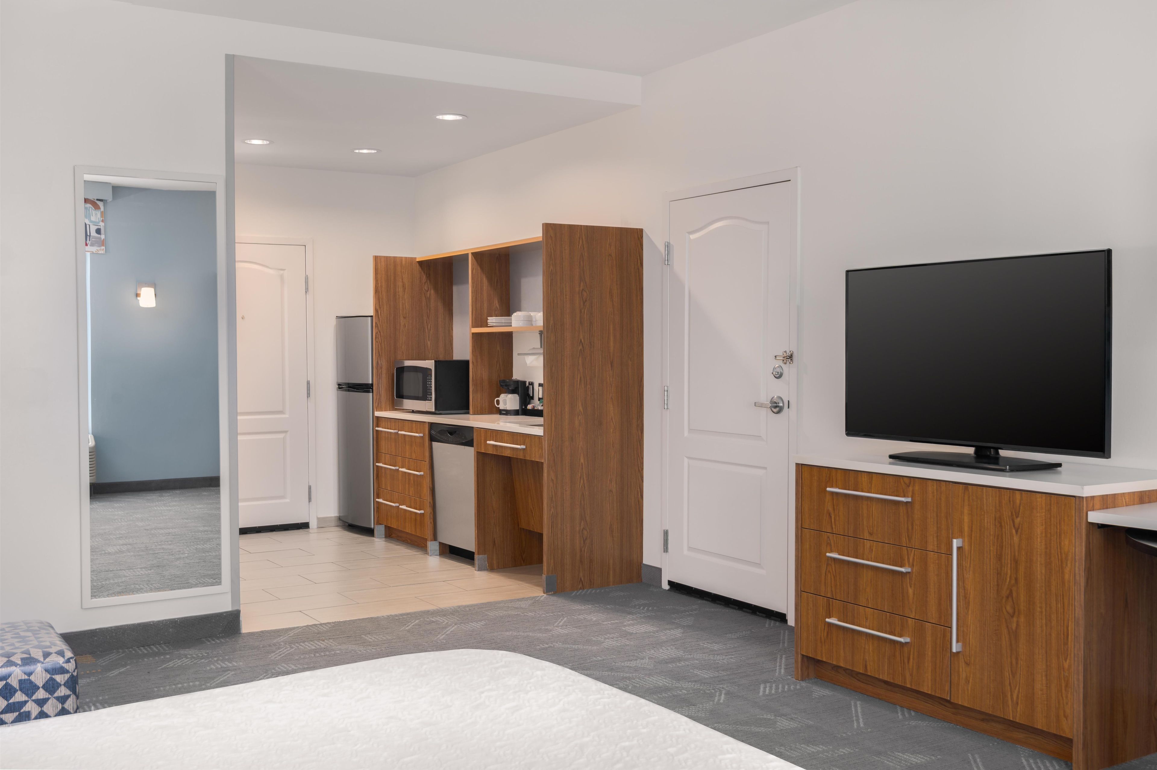 A modern hotel room with a bed, a TV, a kitchenette, and a bathroom.
