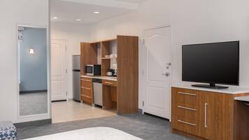 A modern hotel room with a bed, a TV, a kitchenette, and a bathroom.