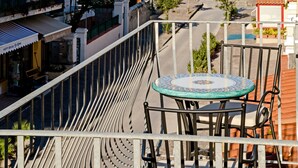 A balcony with a table and chairs overlooking a coastal street with buildings and a sailboat in the distance. - Hotel da Raffaele (Ischia)