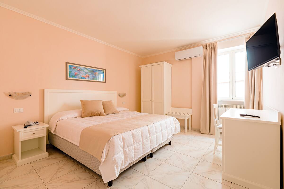 A bedroom with a bed, nightstand, wardrobe, desk, and TV.