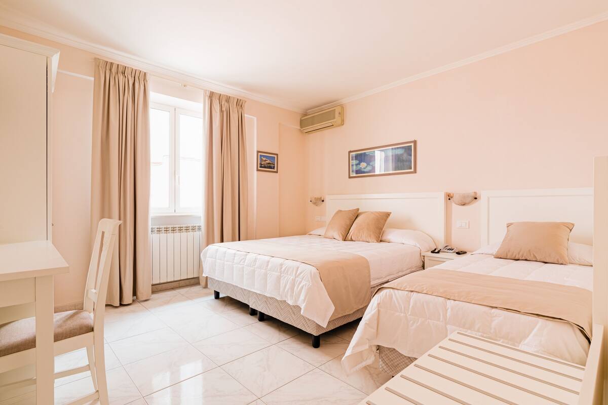 A bedroom with two beds, a chair, a radiator, and a window with curtains.