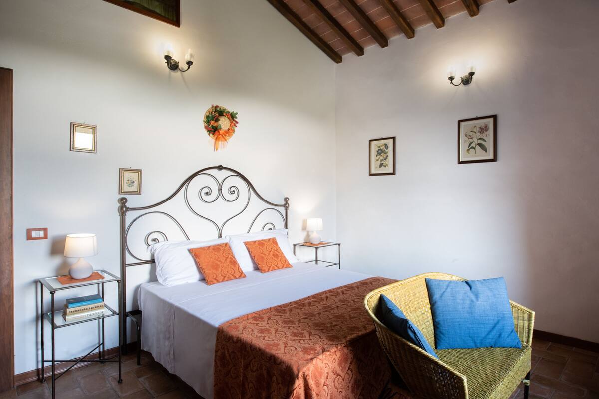 A neatly arranged bedroom with a bed, bedside tables, a chair, and wall-mounted lamps.