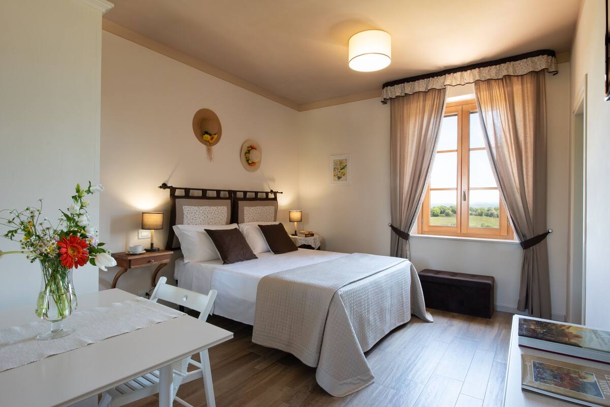 A bedroom with a bed, bedside tables, a desk, and a window with curtains.