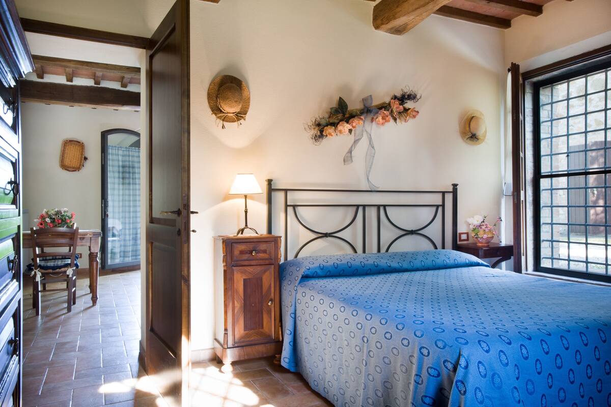 A bedroom with a bed, a nightstand, a lamp, a dresser, a chair, and a window with a view.