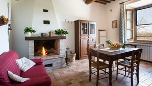Una sala de estar acogedora con chimenea, vigas de madera en el techo, una mesa de comedor con sillas y un ventanal con vistas.