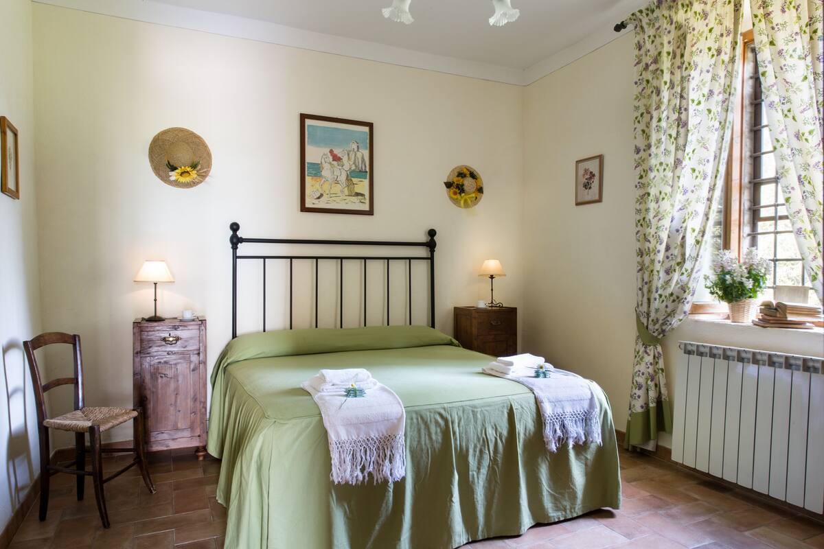 A bedroom with a bed, two bedside tables with lamps, a chair, and a radiator.