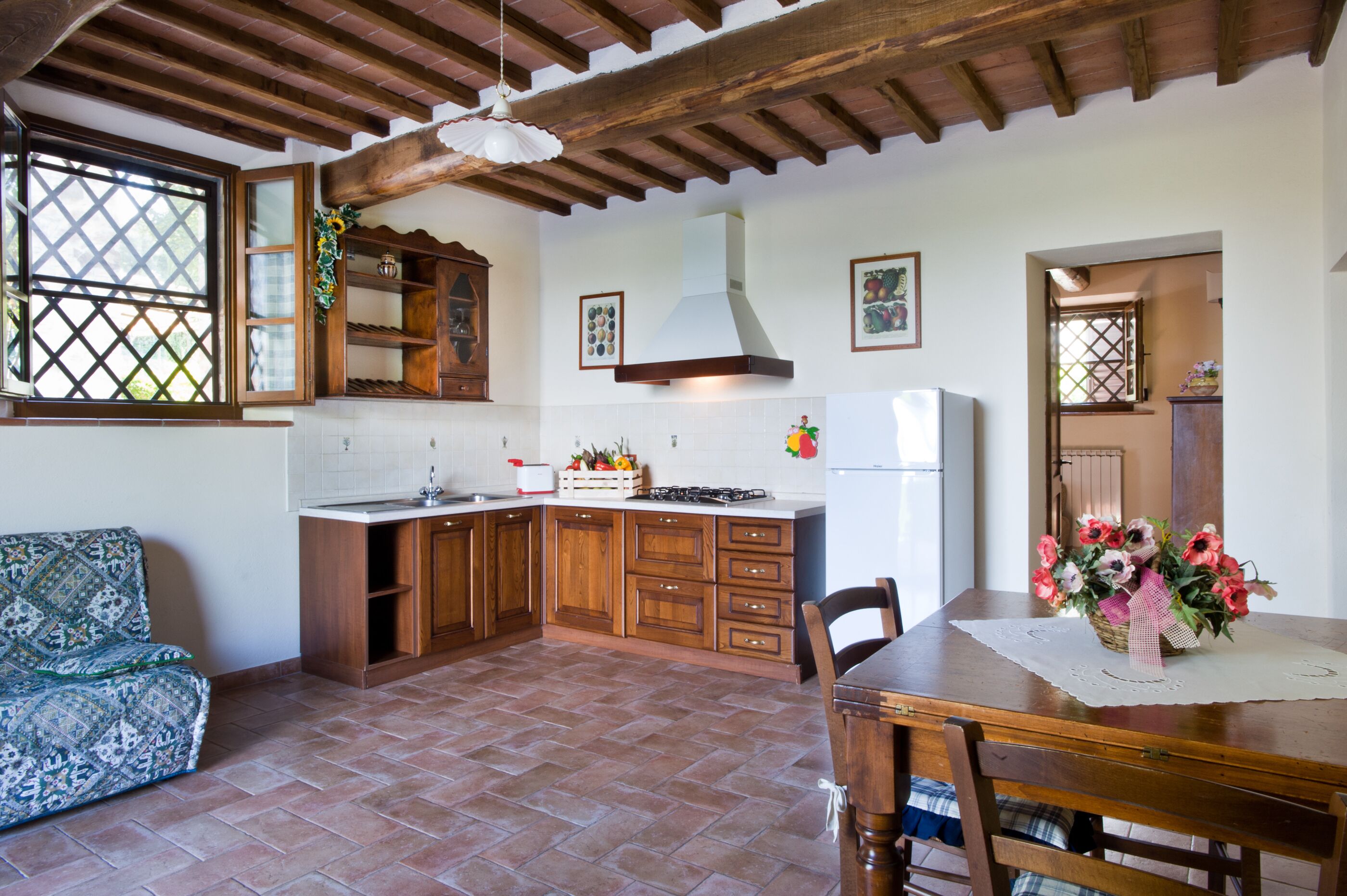 A kitchen with wooden cabinets, a tiled floor, a dining table with chairs, and a refrigerator.