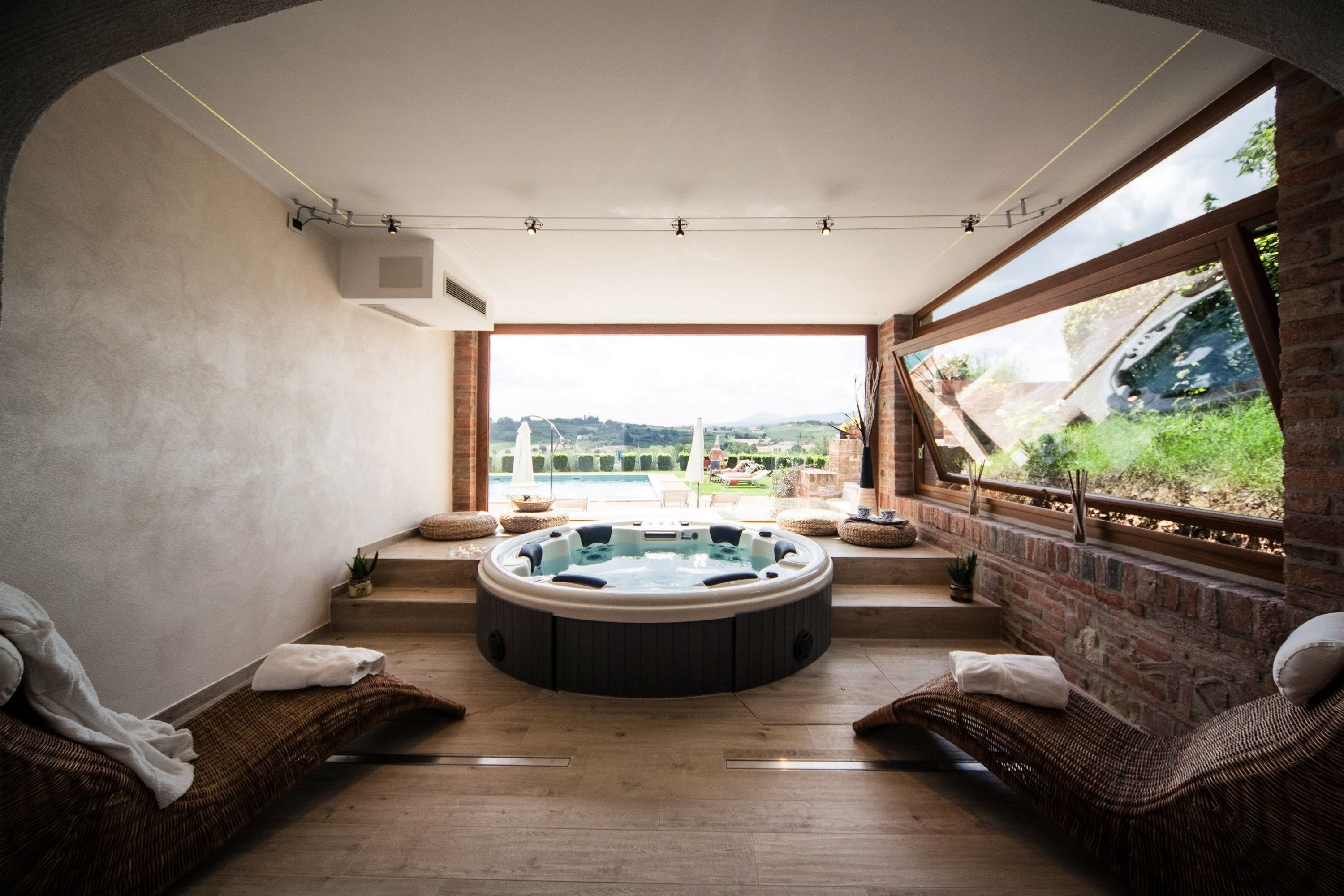 A spa room with a hot tub, wicker seating, and a view of the countryside.