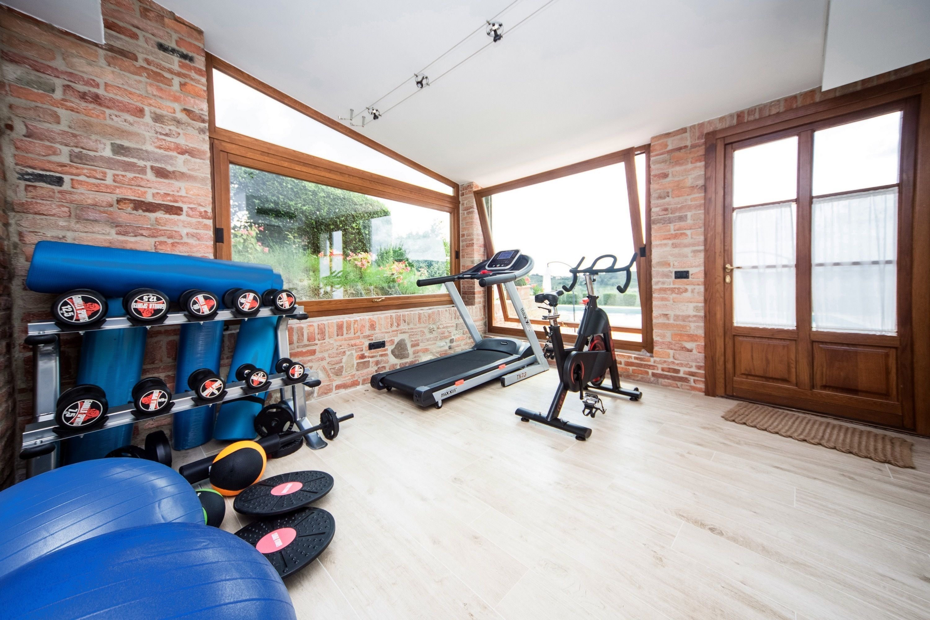 A gym with exercise equipment, a treadmill, and a window with a view of greenery.