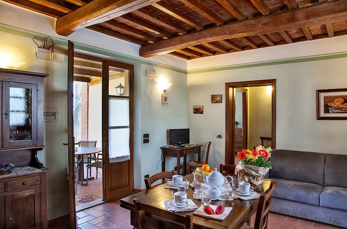 A dining area with a wooden table set for two, a sofa, and a television on a small table.