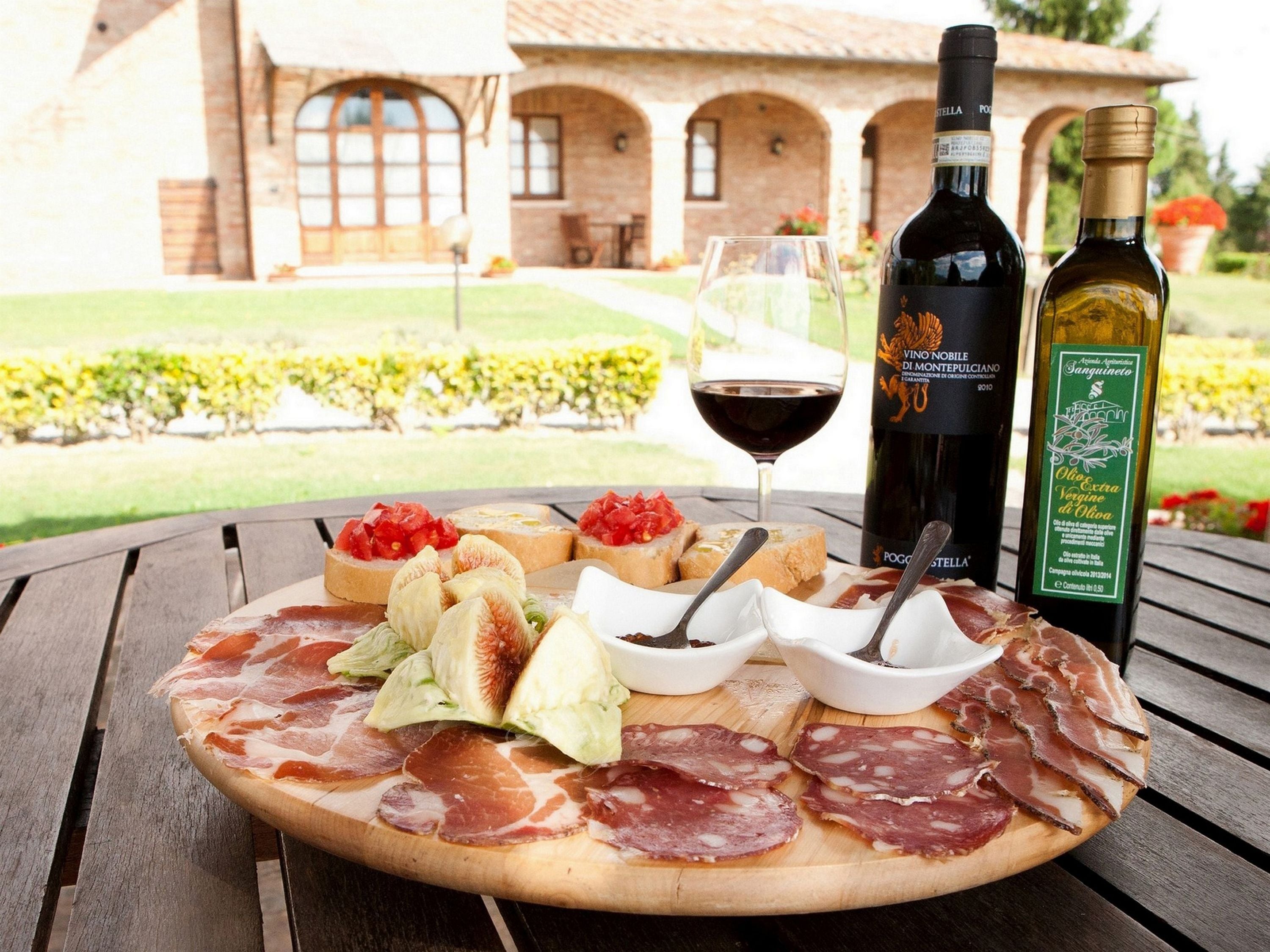 Una mesa de madera con una tabla de embutidos, botellas de vino y una copa de vino tinto.