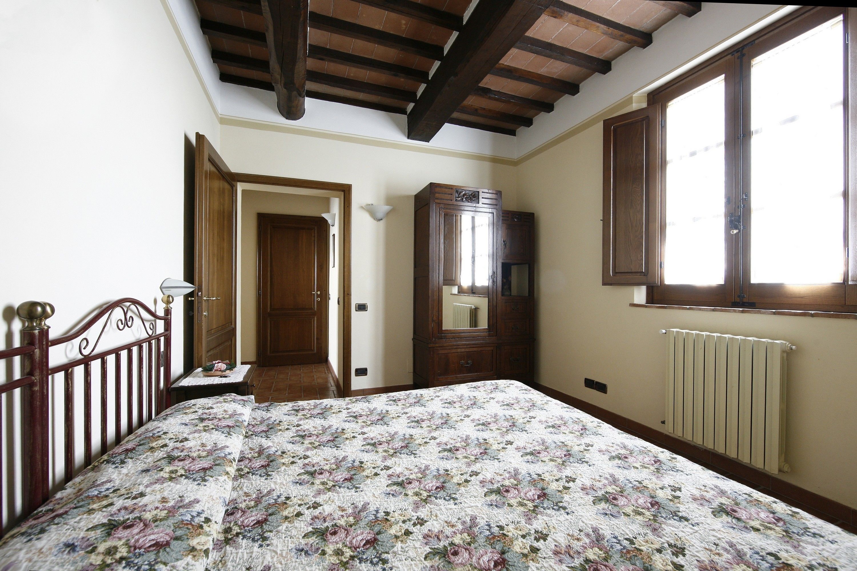 A bedroom with a bed, wooden headboard, a wardrobe, a radiator, and a window.