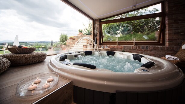 A hot tub with a view of a brick wall and greenery outside.