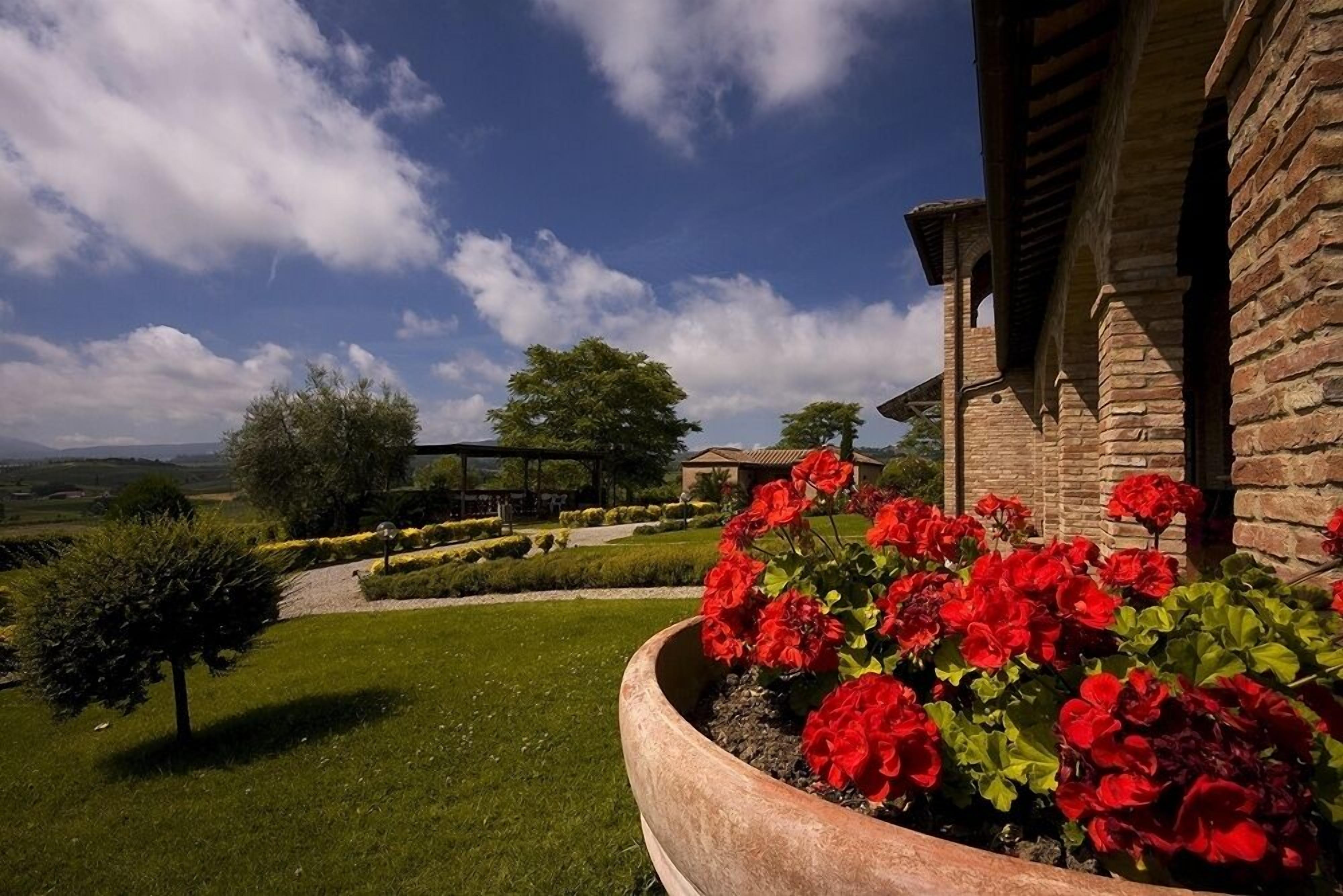 A stone building with a garden featuring red flowers and a well-maintained lawn.