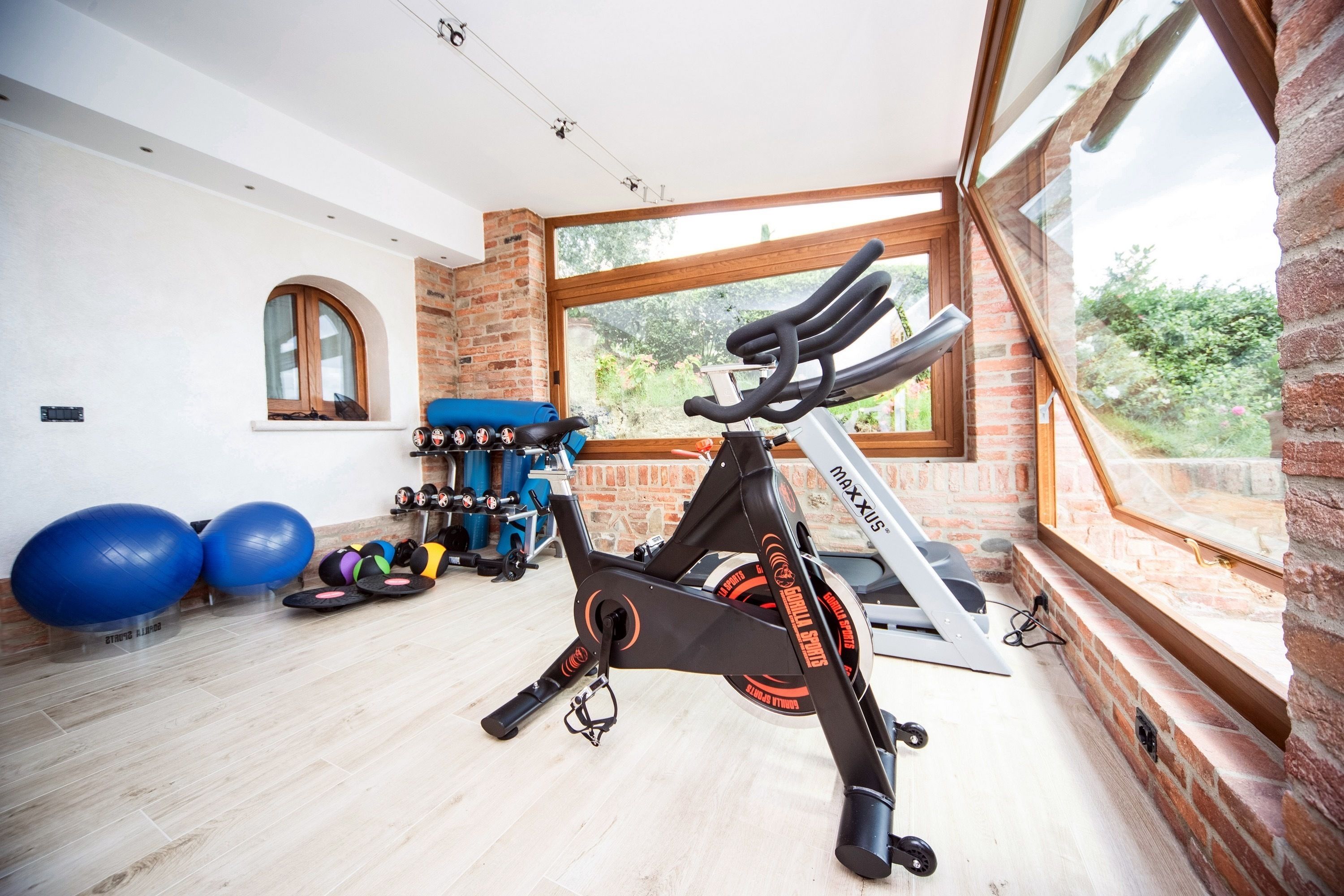 Un gimnasio en casa con equipo de ejercicio, un ventanal grande y una pared de ladrillo.