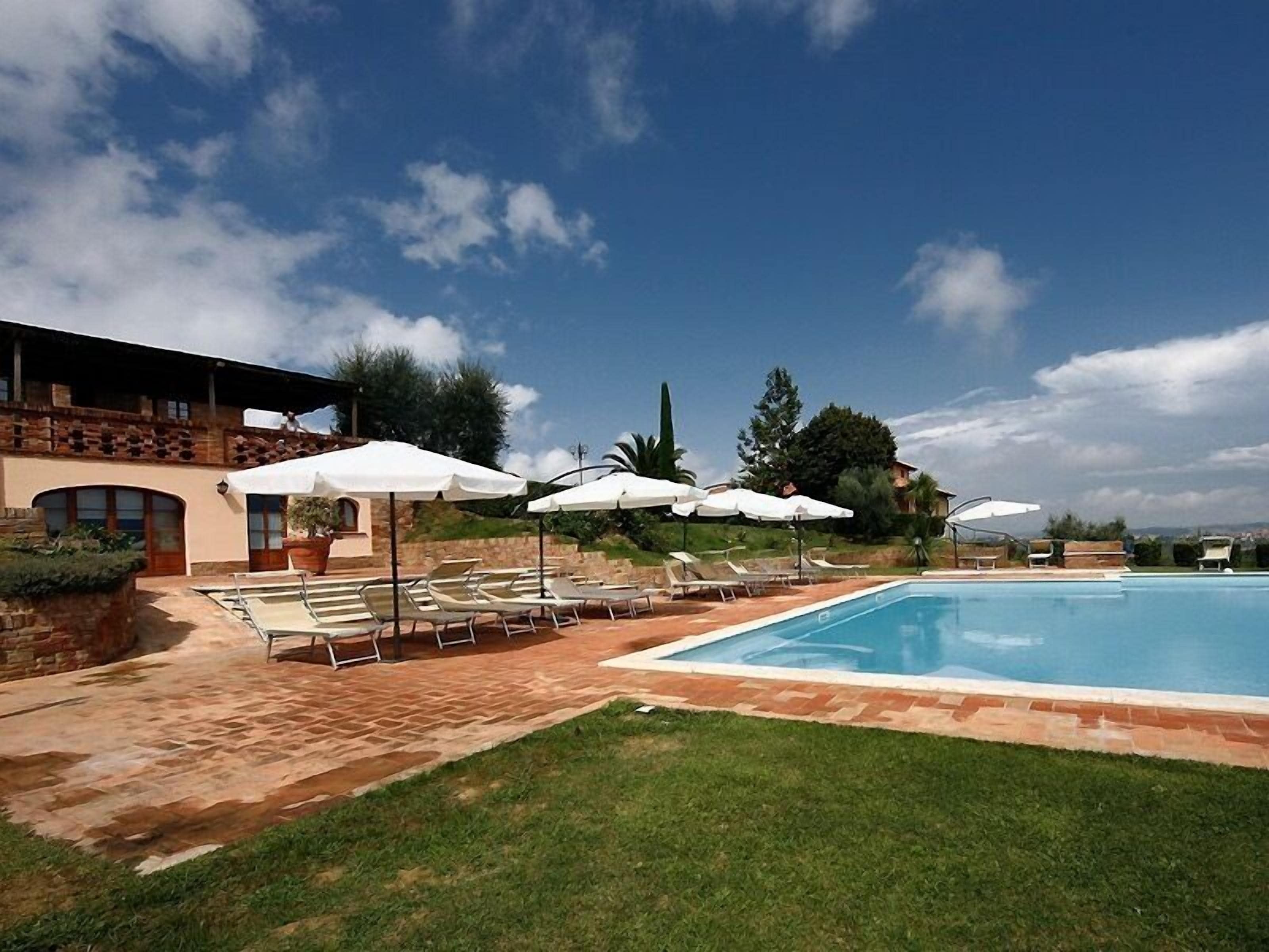 A pool area with lounge chairs and umbrellas, a stone building, and a clear sky.